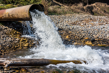 close up of a large pipe with water flowing into a stream