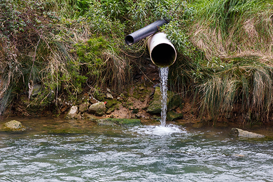 a large and small pipe both pumping water into a stream 